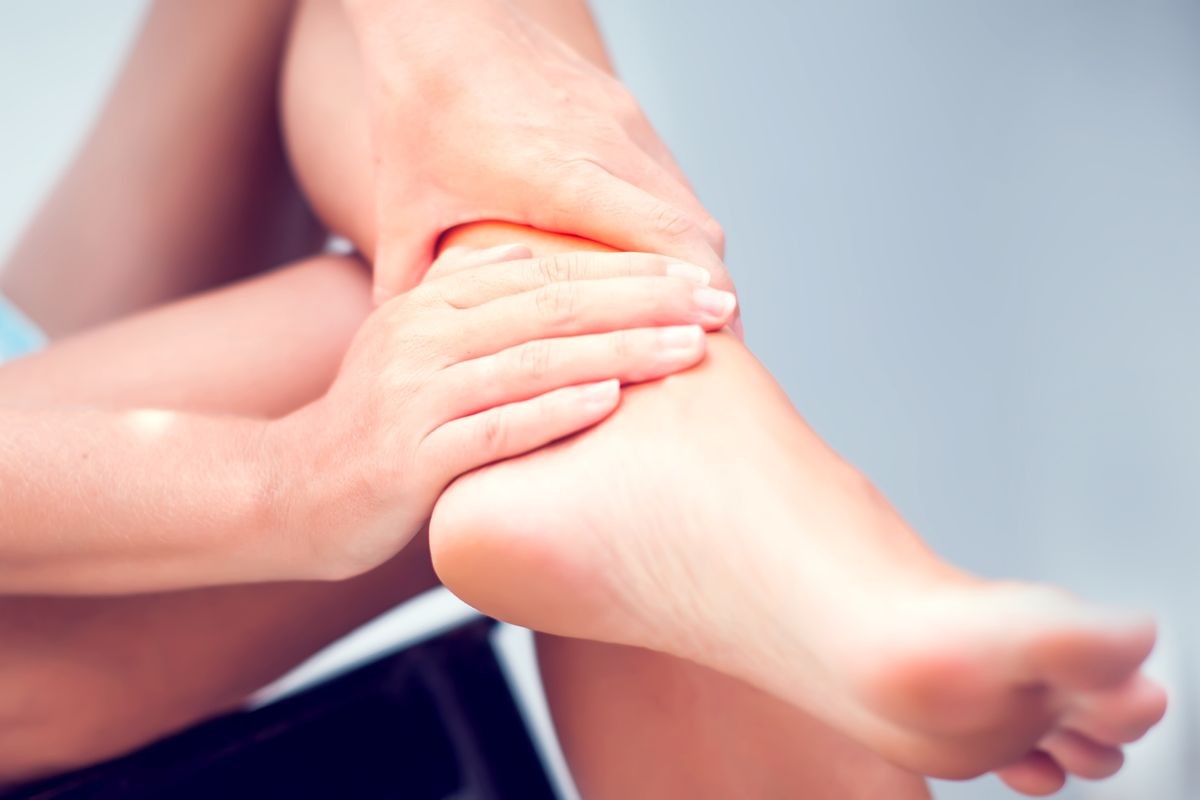 Pain in the foot, girl holds her hands to her feet, foot massage, cramp, muscular spasm, red accent on the foot, close-up